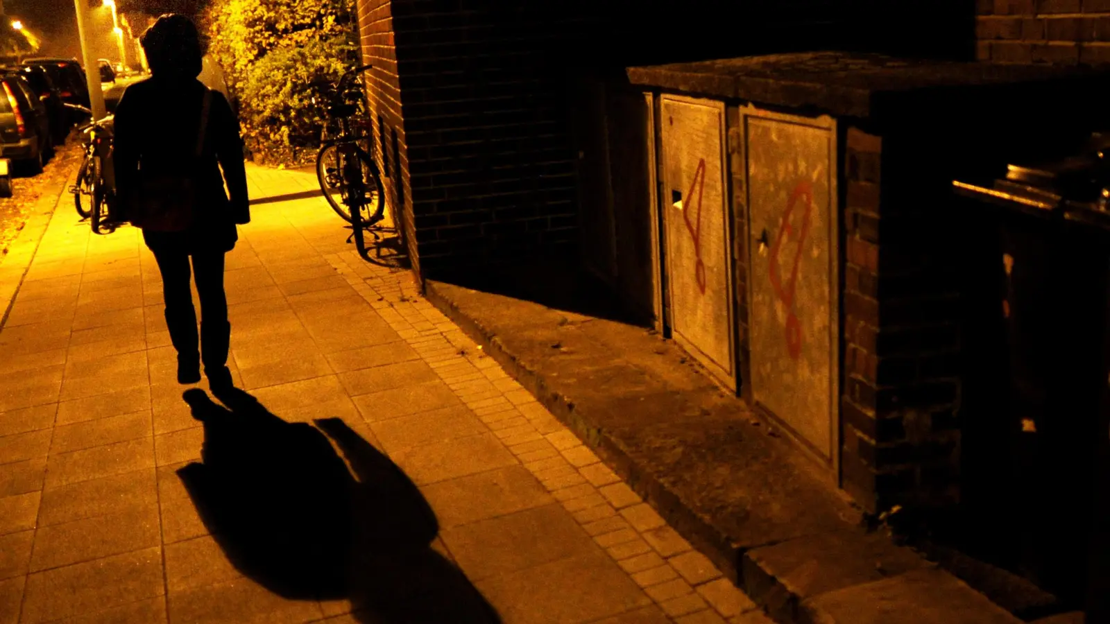 Eine Frau geht im Licht der Straßenlaternen über eine Straße.  (Symbolbild: Julian Stratenschulte/dpa)