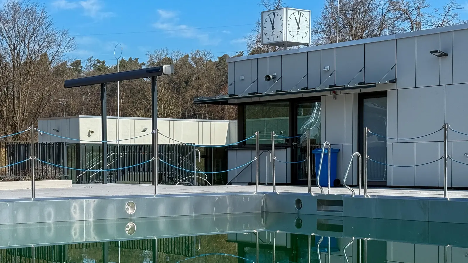 Während in den Becken noch eine grünliche Brühe vor sich hindümpelt, ist die neue Analog-Uhr am Dach des Bademeisterhauses schon mal installiert – und bereit für die Badöffnung in einigen Wochen. (Bild: Wolfgang Steinbacher)