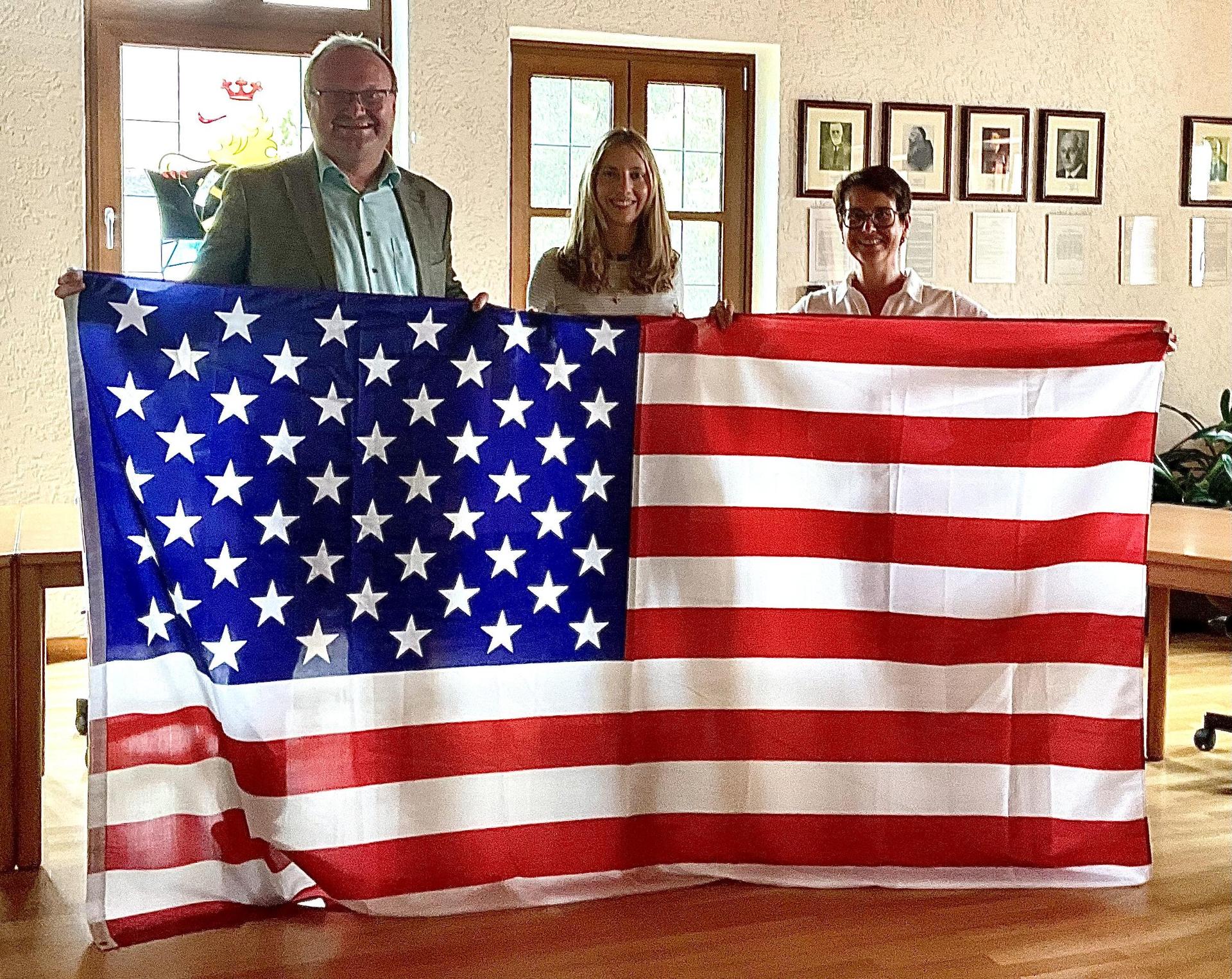 Die Juniorbotschafterin Paula Dotzler (Bildmitte) mit Bürgermeister Uwe König und Bundestagsabgeordneter Susanne Hierl zeigen mit der Flagge der USA an, wo es für Paula hingeht (Bild: Gerhard Krones)
