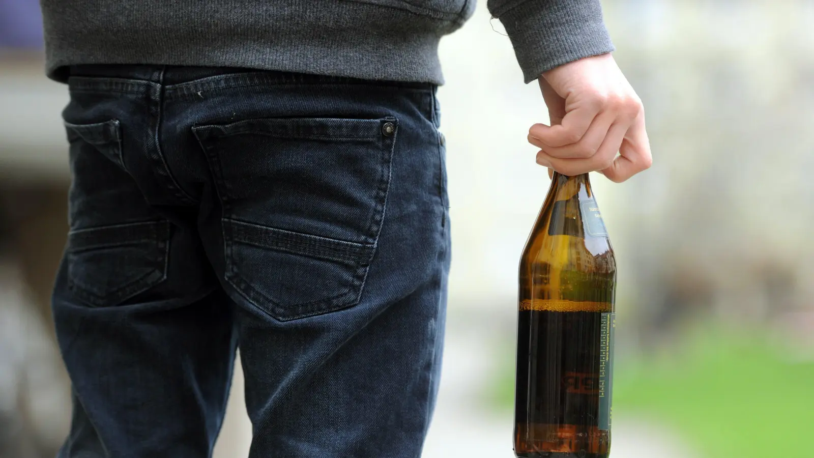 Eine Person hält eine geöffnete Bierflasche in der Hand. In Regensburg hat ein 29-Jähriger mit einer geworfenen Flasche eine Frau im Gesicht verletzt. (Symbolbild: Tobias Hase /dpa)