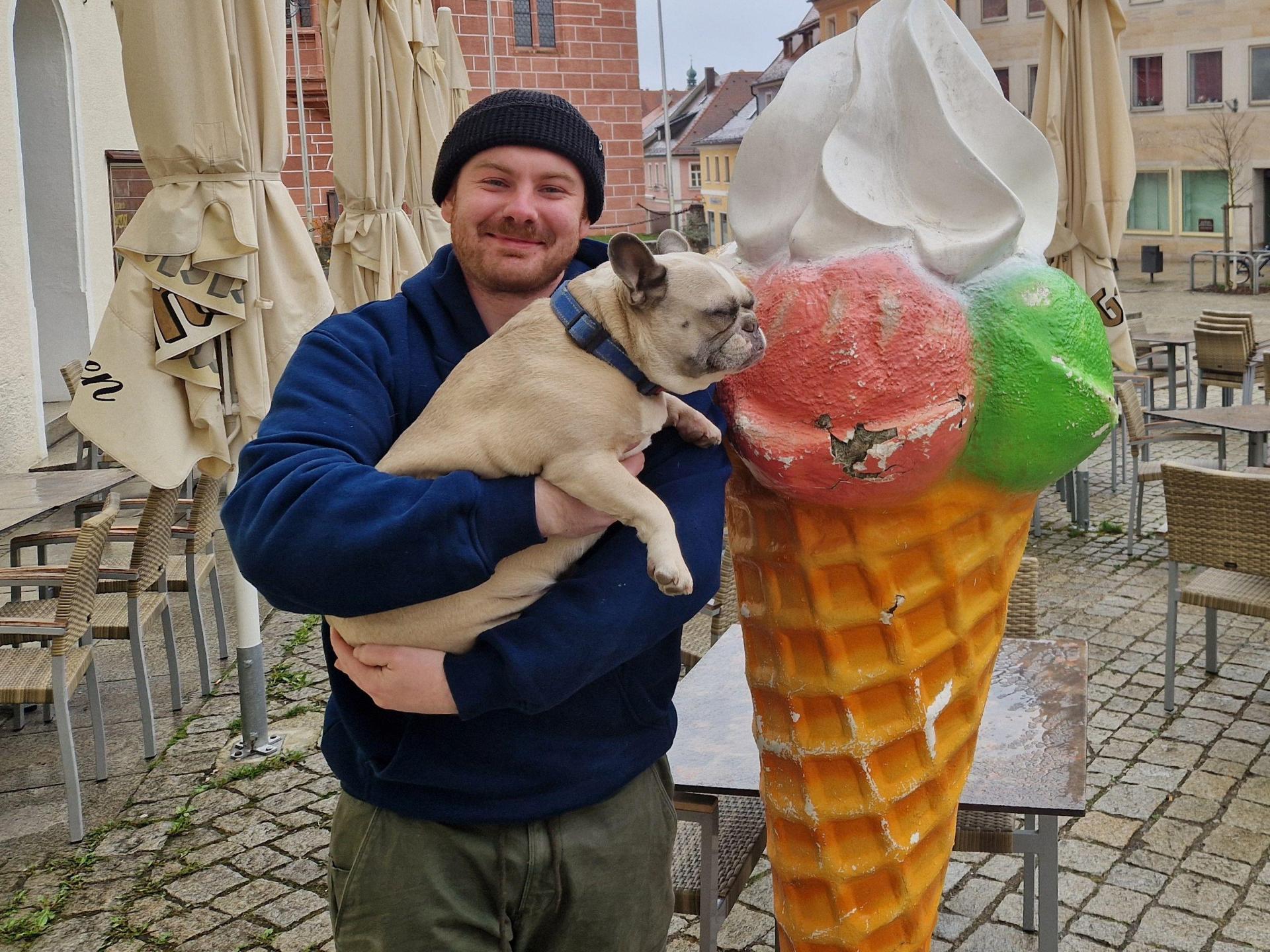 Wenn schon ständig Leute für ein Selfie kommen, muss der „Chef” auch mal auf ein Foto mit „Sulzbachs berühmtester Eistüte”: Wirt Tim Biersack, mit seiner französischen Dogge Heidi, freut sich, dass sein geklauter Werbeaufsteller wieder da ist. (Bild: Tobias Gräf)